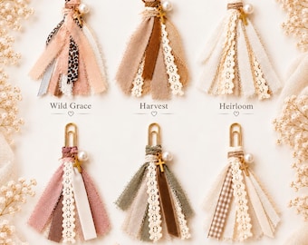 May include: Six decorative paper clips with fabric tassels in various colors and textures. Each tassel features a gold-tone cross charm and a white faux pearl bead. The styles are labeled Wild Grace, Harvest, Heirloom, Grace, Give Thanks, and Quiet Time with Jesus.