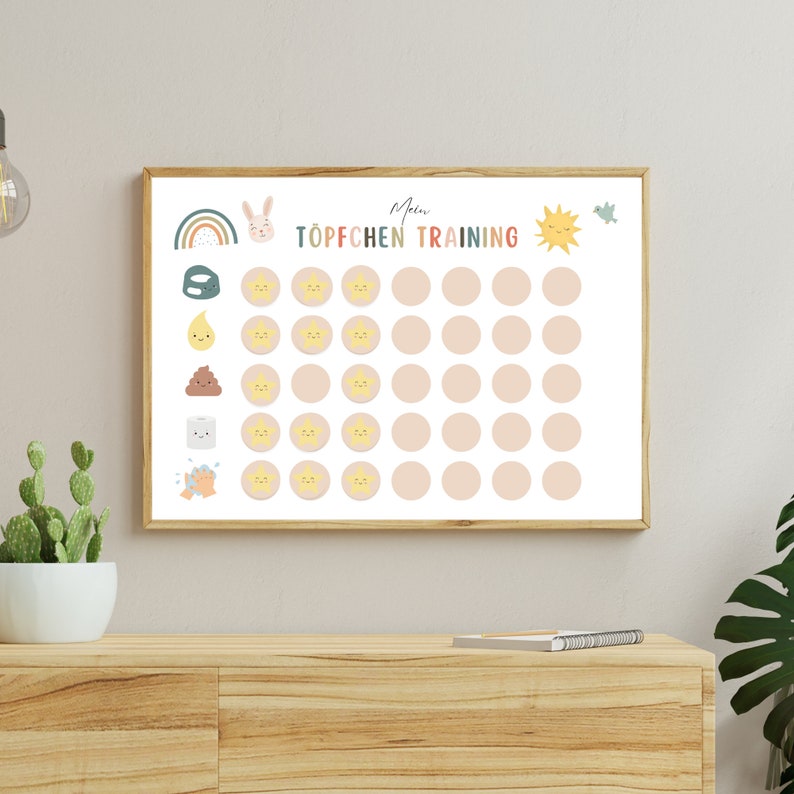May include: A white poster with a light pink background and a wooden frame. The poster has a rainbow, a bunny, a sun, a bird, and a toilet. The poster says "Mein T&ouml;pfchen Training".