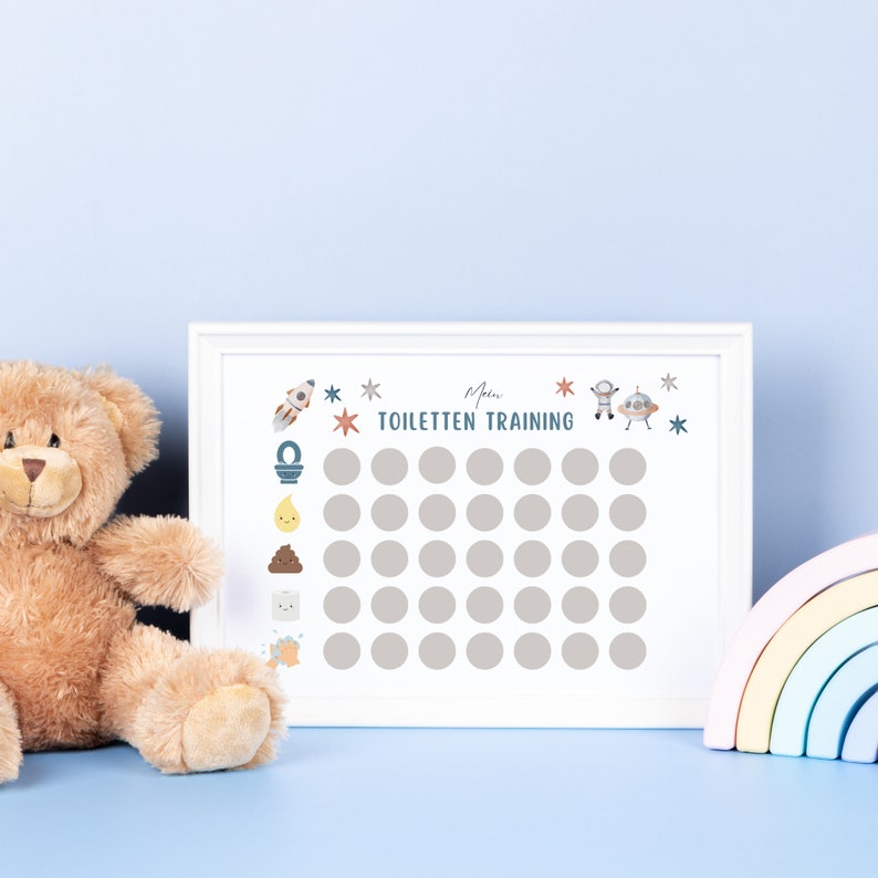 K&ouml;nnte beinhalten: Ein wei&szlig;er gerahmter Chart mit dem Text "Mein Toiletten Training" und einem Raster mit 36 Kreisen. Der Chart hat eine Rakete, eine Toilette, ein Kack-Emoji, ein H&auml;ndewaschen-Symbol und ein Raumschiff darauf. Ein Teddyb&auml;r und ein Regenbogenspielzeug befinden sich im Vordergrund.