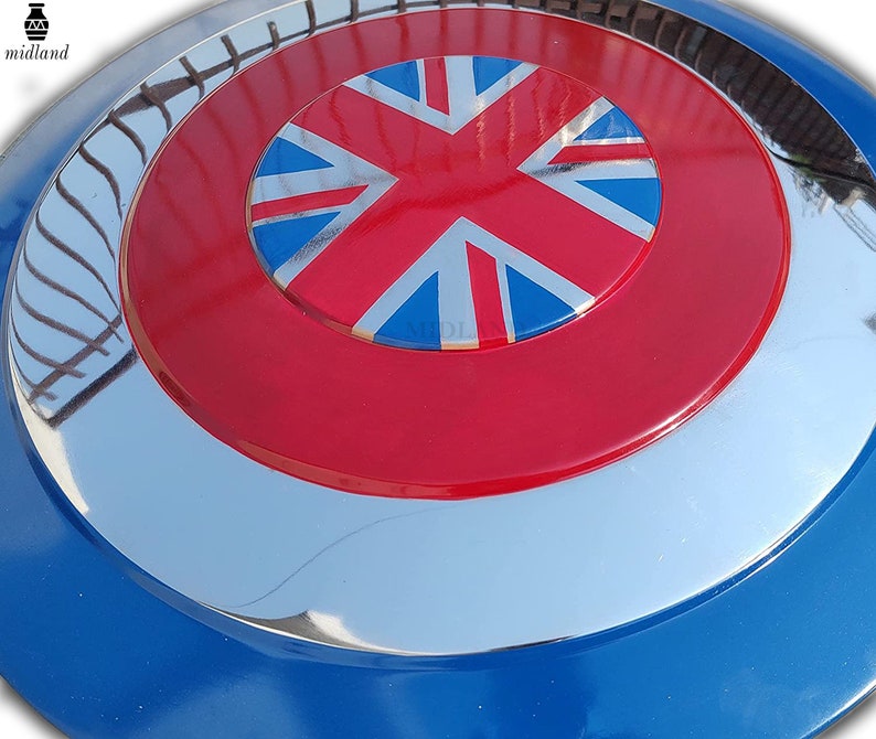 May include: A circular shield with a blue, silver, red, and white design. The centre features a red circle with a Union Jack flag. The shield has a reflective, metallic finish.