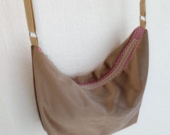 May include: A brown suede shoulder bag with a tan strap. The bag has a zipper closure with a pink polka dot lining. The strap is attached to the bag with silver metal rings.
