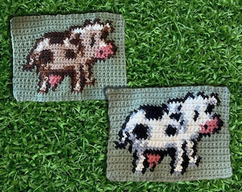 May include: Two crocheted cow squares, one with brown and white spots and the other with black and white spots. Both cows have pink noses and are on a green background.