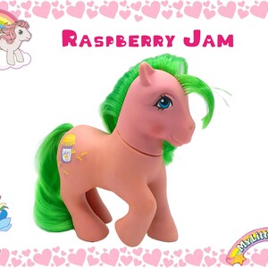 May include: A pink My Little Pony toy with green hair and a yellow and white jar on its side. The pony has blue eyes and a pink nose. The pony is standing on a white background with a pink heart border.