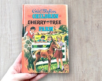 May include: Vintage hardcover book titled "The Children of Cherry Tree Farm" by Enid Blyton. The cover features a colorful illustration of children with a pony on a farm, set against a light orange background.