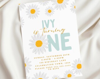 May include: A white invitation with a blue and yellow daisy design. The text reads "Ivy is turning one" with a blue and white "one" in large font. The invitation includes details for a birthday party on Sunday, September 28th from 2:00 PM to 4:00 PM. The address is 123 Birthday Lane, Celebration Town, 1234. The RSVP information is "Please text 555-555-5555".