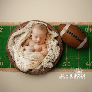 Könnte beinhalten: Ein neugeborenes Baby schläft in einer braunen Schüssel, die mit weißem Garn gefüllt ist, vor einem grünen und weißen Fußballfeld-Hintergrund. Ein brauner Fußball befindet sich rechts neben der Schüssel.