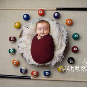 May include: A baby swaddled in a burgundy blanket is lying in a wooden bowl surrounded by billiard balls. A pool cue is laying across the top of the image. The text "Liz Hibiscus Digital Backdrops" is in the bottom right corner of the image.