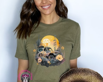 May include: A green t-shirt with a graphic of a jeep driving through a forest at night with a full moon in the background. The graphic is surrounded by flowers and foliage.