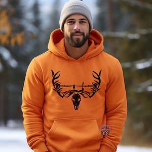 May include: Orange hoodie with a black deer skull and antlers graphic. The graphic also includes a bow and arrow.