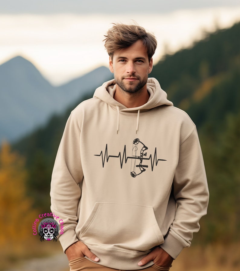May include: A beige hoodie with a black graphic of a bow and arrow inside a heartbeat. The hoodie has a drawstring hood.
