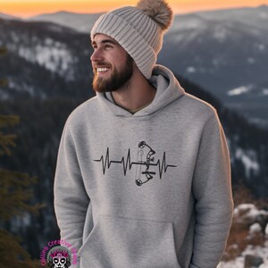 May include: A gray hoodie with a black and white graphic of a bow and arrow inside a heartbeat. The hoodie has a hood and a pouch pocket.