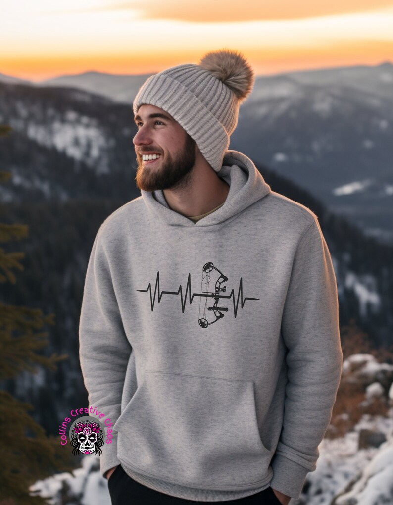 May include: A gray hoodie with a black and white graphic of a bow and arrow inside a heartbeat. The hoodie has a hood and a pouch pocket.