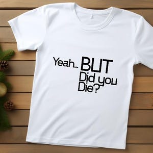 May include: White crew neck t-shirt with the text "Yeah... BUT Did you Die?" in black. The shirt is on a wooden background with a Christmas tree branch with gold and red ornaments.
