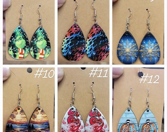 Puede incluir: Seis pares de pendientes en forma de lágrima con varios diseños. Incluyen un Grinch, patrones coloridos, copos de nieve, una puesta de sol, la palabra "HOPE" con una cinta rosa y una calabaza con estampado de leopardo.