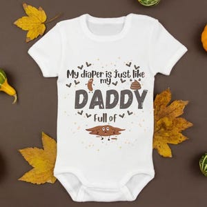 Puede incluir: Body de bebé blanco con el texto "My diaper is just like my DADDY full of" e ilustraciones de caca. El body está rodeado de hojas de otoño y calabazas.