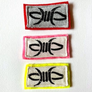 Puede incluir: Tres parches rectangulares con un diseño de alambre de púas negro. Cada parche tiene un borde de color diferente: rojo, rosa y amarillo. El diseño de alambre de púas está centrado en un fondo blanco o gris.