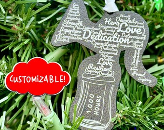May include: A gray wooden ornament shaped like a spray paint can with the words "Dedication", "Love", "Resilient", and "1,000 Hours" printed on it. The ornament is decorated with a cloud-shaped tag that says "CUSTOMIZABLE!" in red.