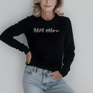 May include: A black long-sleeved sweatshirt with the word "Black" spelled out in American Sign Language.
