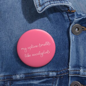 May include: A bright pink button with the text "my upline smells like eucalyptus" in white script. The button is set against a blue denim jacket.