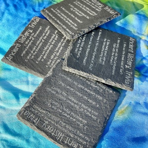 May include: Four black slate coasters with white text. Each coaster features a different set of trivia questions about ancient history. The text on the coasters includes questions about the Great Pyramid of Giza, the Colosseum, the Roman Empire, and the Greek God of War.