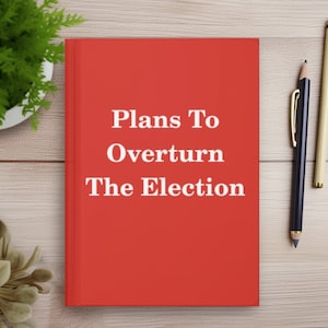 May include: A red hardcover book with the title "Plans To Overturn The Election" printed in white on the front cover. The book is lying on a wooden surface with two pencils beside it.