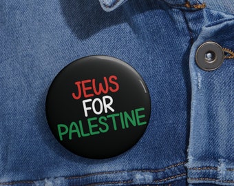 Könnte beinhalten: Ein schwarzer Knopf mit dem Text "JEWS FOR PALESTINE" in weißer, roter und grüner Schrift. Der Knopf ist an einer blauen Jeansjacke befestigt.