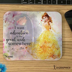 May include: A mousepad featuring a watercolor illustration of Belle from Beauty and the Beast. The background is a soft pink and purple with a quote that reads "I want adventure in the great wide somewhere." The quote is in black cursive font and is signed "Belle".