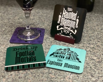 Könnte beinhalten: Vier Untersetzer mit einem gruseligen Thema. Ein Untersetzer ist schwarz mit weißem Text, der "The Haunted Mansion" lautet. Ein weiterer Untersetzer ist grün mit schwarzem Text, der "Drink Up Foolish Mortals" lautet. Ein dritter Untersetzer ist blau mit schwarzem Text, der "The Espinosa Mansion" lautet. Der vierte Untersetzer ist lila mit einem schwarzen Design.