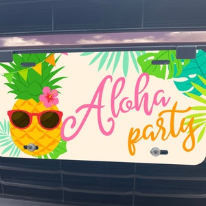 May include: License plate with a tropical theme. It features a yellow pineapple wearing sunglasses and a pink flower, with the words "Aloha party" in pink and orange. Green and blue tropical leaves surround the pineapple.