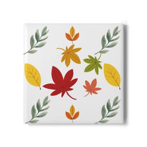 May include: A square white tile featuring a repeating pattern of autumn-themed illustrations, including red, yellow, and orange maple leaves, green foliage sprigs, and small golden-brown leaf clusters arranged across the surface.