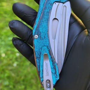 May include: A folding pocket knife with a teal and brown handle and a silver blade. The handle has a textured, weathered appearance. The knife has a silver pocket clip with the brand name "Kershaw" engraved on it.