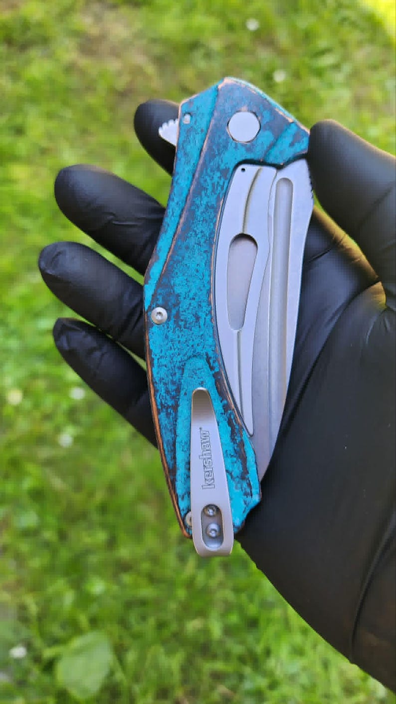 May include: A folding pocket knife with a teal and brown handle and a silver blade. The handle has a textured, weathered appearance. The knife has a silver pocket clip with the brand name "Kershaw" engraved on it.