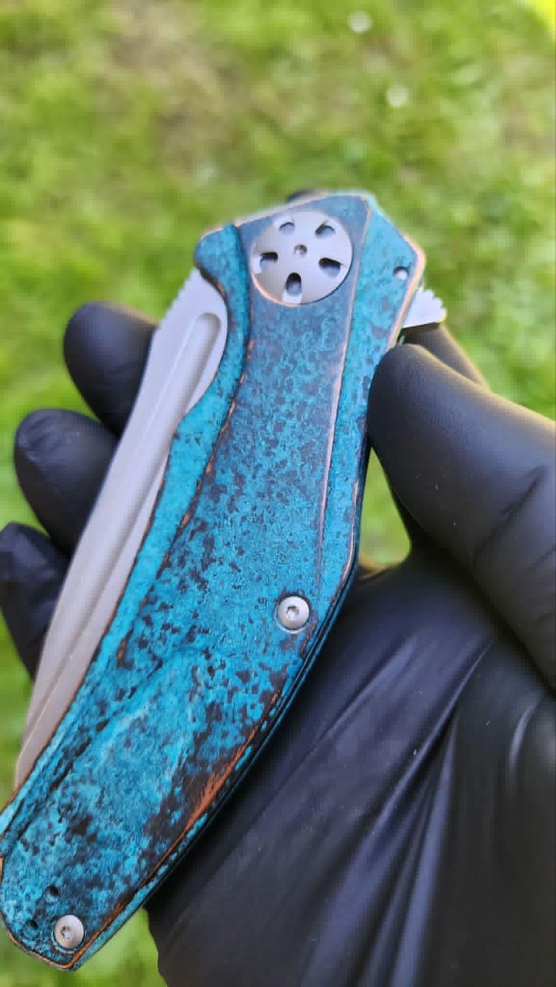 May include: A folding pocket knife with a weathered, turquoise and brown handle. The blade is silver, and the handle has a textured, aged appearance. The knife is held against a blurred green background.