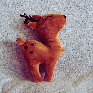 May include: A plush, brown deer toy with dark brown antlers and black spots. The deer has closed eyes and a small, black nose. The toy is made of soft material and is likely intended for children.