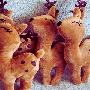 May include: A group of plush reindeer toys in various poses. The reindeer are a warm brown color with darker brown antlers and black eyes. Some have dark purple spots on their bodies. The toys are soft and cuddly, perfect for holiday decor.