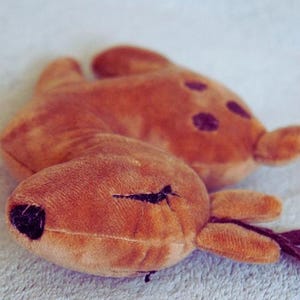 May include: Two plush deer toys in shades of brown. One deer is in the foreground with a black nose and stitched eye. The other deer is slightly out of focus in the background, with dark spots on its back.
