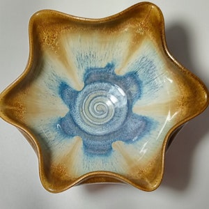 May include: A star-shaped ceramic bowl with a blue and white glaze. The bowl has a wavy rim and a spiral design in the center.