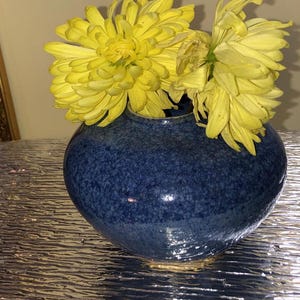 May include: A blue ceramic vase with a speckled glaze holds a bouquet of yellow chrysanthemums.