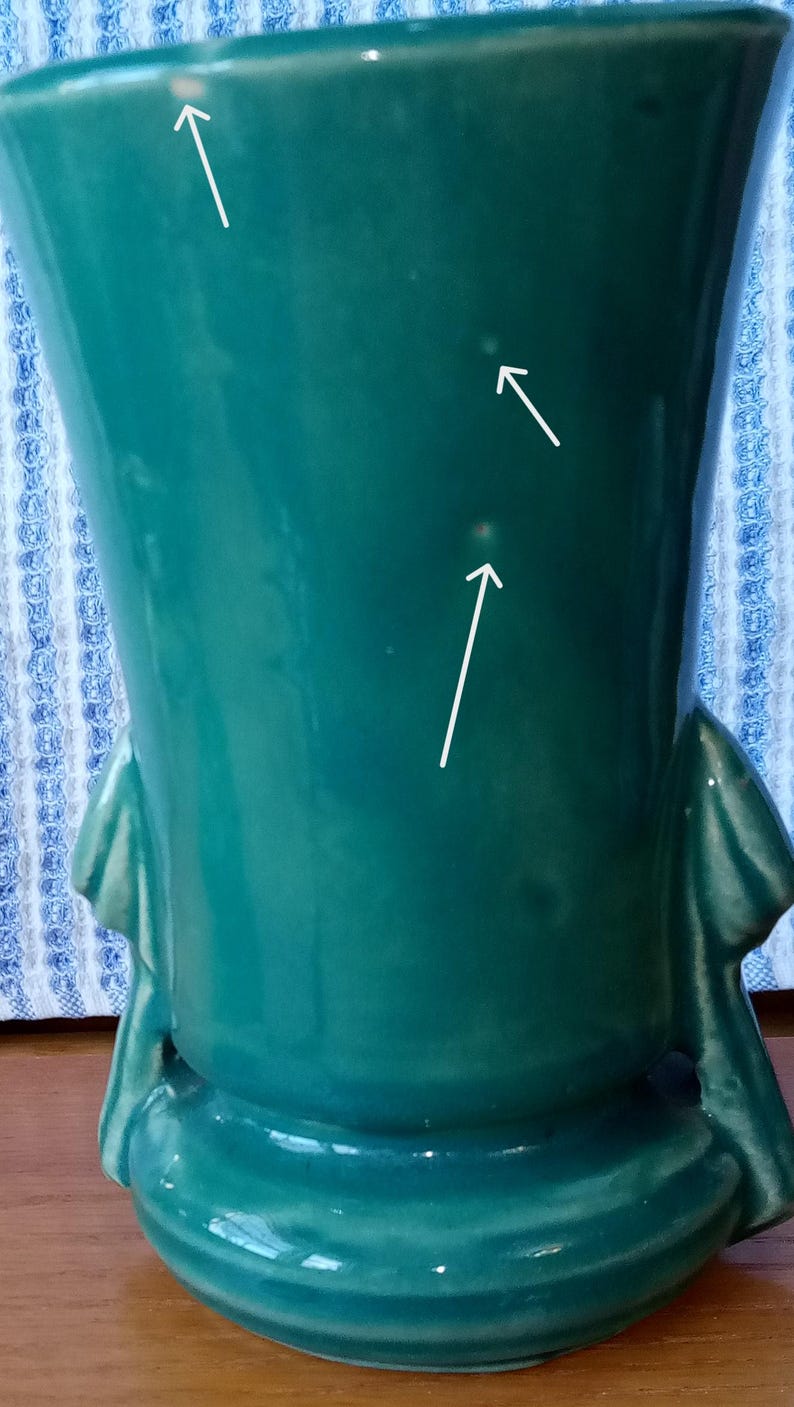 May include: A teal green ceramic vase with two handles. The vase has three small white spots on the surface.