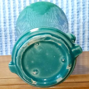 May include: A teal green ceramic vase with a rounded bottom and a flared top. The vase has a smooth, glossy finish.