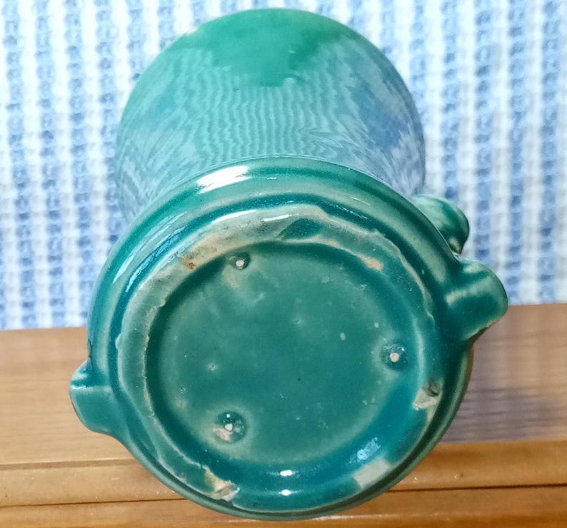 May include: A teal green ceramic vase with a rounded bottom and a flared top. The vase has a smooth, glossy finish.