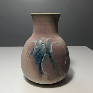 May include: A ceramic vase with a rounded body and a narrow neck. The vase is decorated with a swirling pattern of blue, white, and pink glaze.