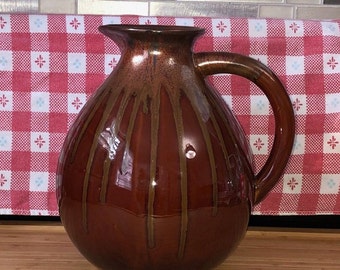 May include: A brown ceramic jug with a wide mouth and a handle. The jug has a glossy finish and brown glaze with vertical brown stripes.