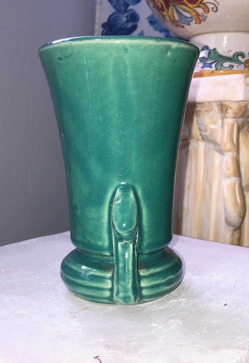 May include: A green ceramic vase with a flared top and a sculpted base. The vase has a smooth, glossy finish.