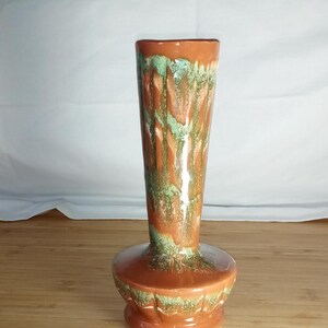 May include: A brown and green ceramic vase with a flared base and a tall, slender neck. The vase has a mottled glaze with shades of brown, green, and white.