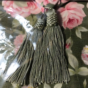 May include: A pair of green tassel tiebacks with a floral print background. The fabric features pink and white roses. The text "HOME TRENDS" is printed on the top of the image.
