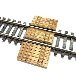 May include: Three wooden planks with a textured surface and a pattern of small squares. The planks are placed on top of a model railway track.