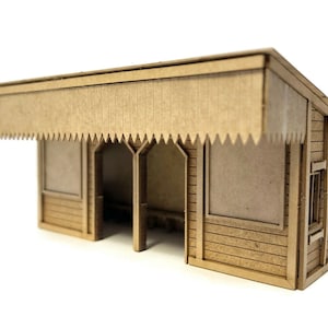 May include: A cardboard model of a small railway station with a brown wooden exterior and a roof with a decorative overhang. The station has two windows and a door.