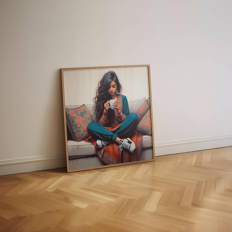 May include: A framed art print shows a person seated on a sofa, holding a white mug. The person wears teal trousers, a rust-coloured top, and white trainers. The sofa has floral cushions and a red patterned blanket. The artwork is in a wooden frame.