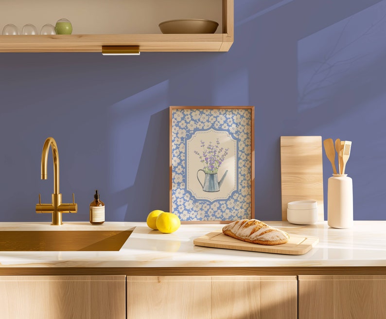 May include: A kitchen scene featuring a framed floral print with a watering can, a loaf of bread on a cutting board, and a gold faucet. The countertop has lemons and a bottle of soap. The background is a solid blue wall.